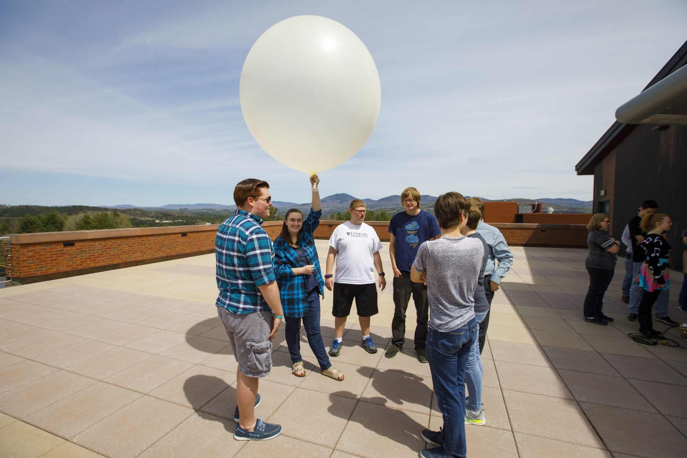 Atmospheric science students stand on the observation deck preparing to launch a weather balloon.