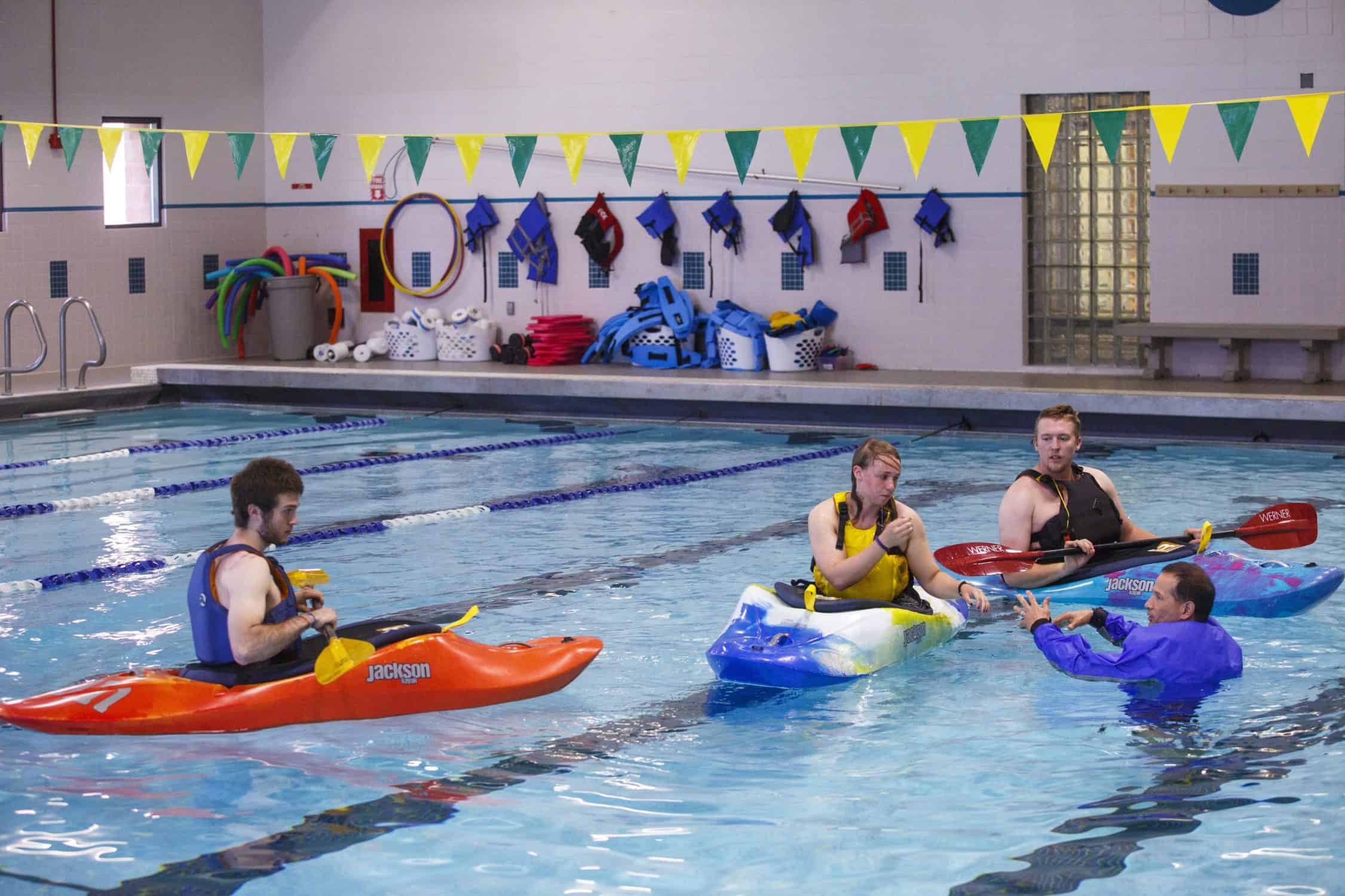 Students use kayaks in the pool on campus with their professor