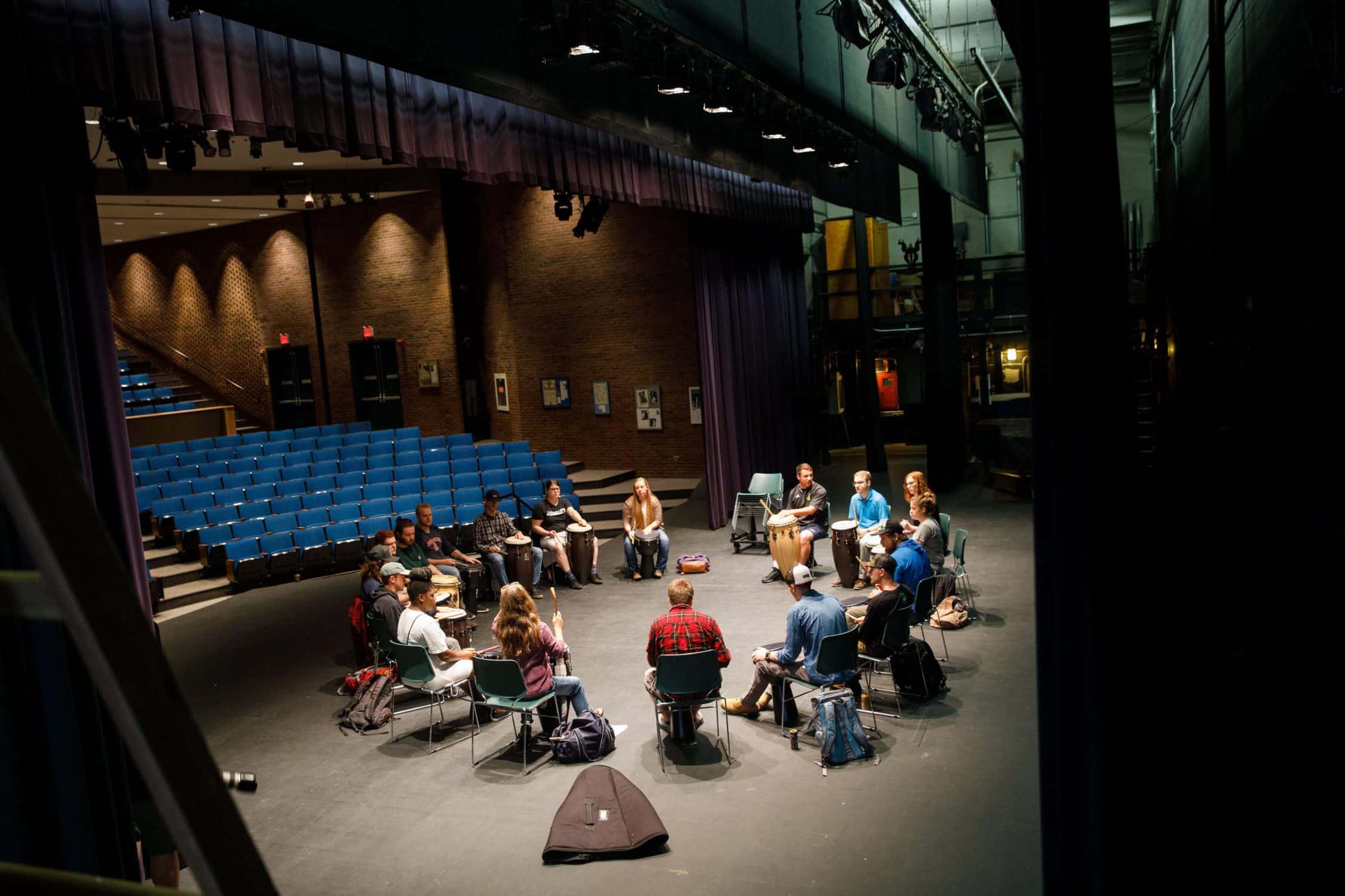 Students sit in a circle with drums
