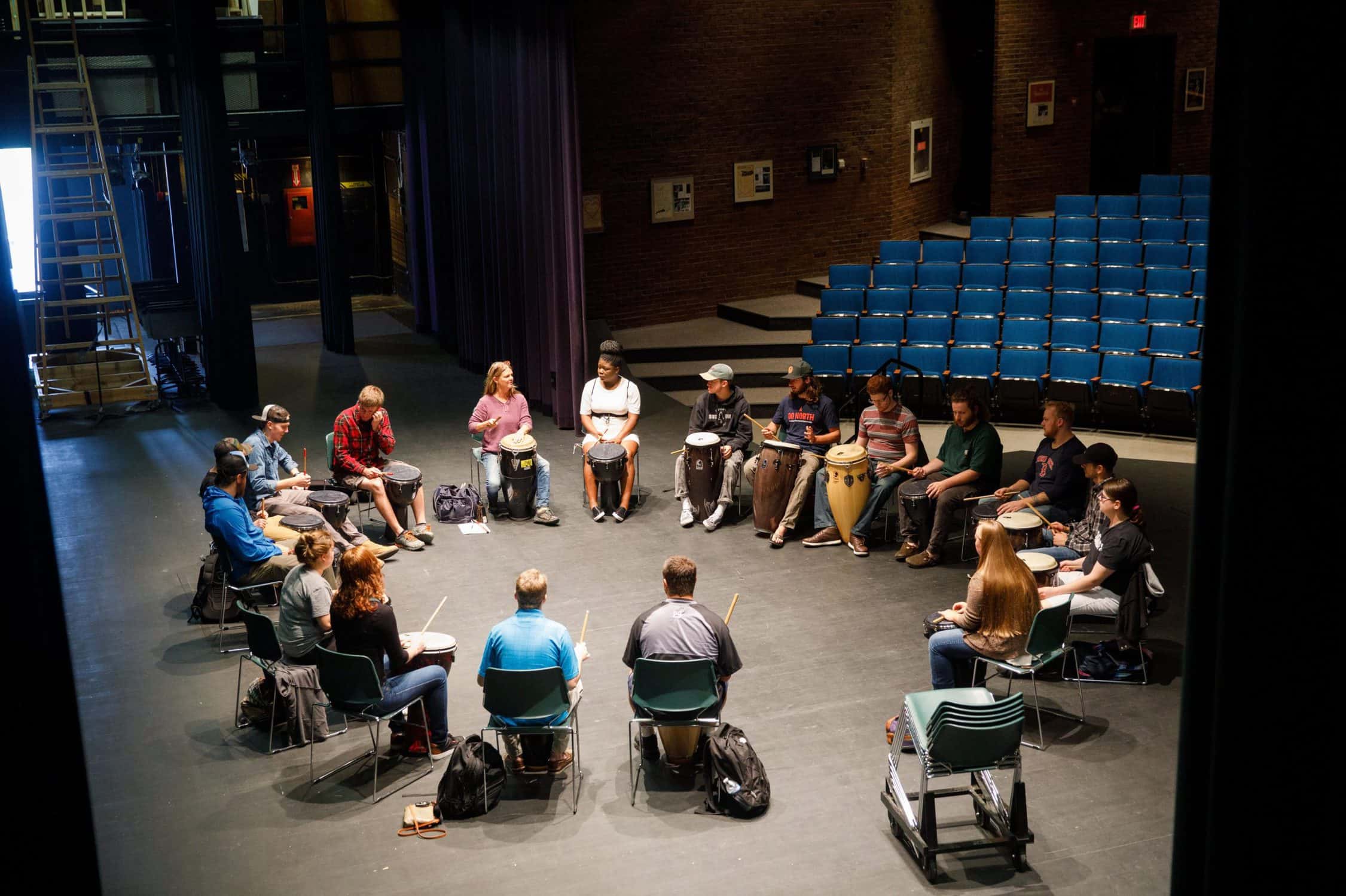 On the stage, students gather in a circle with drums