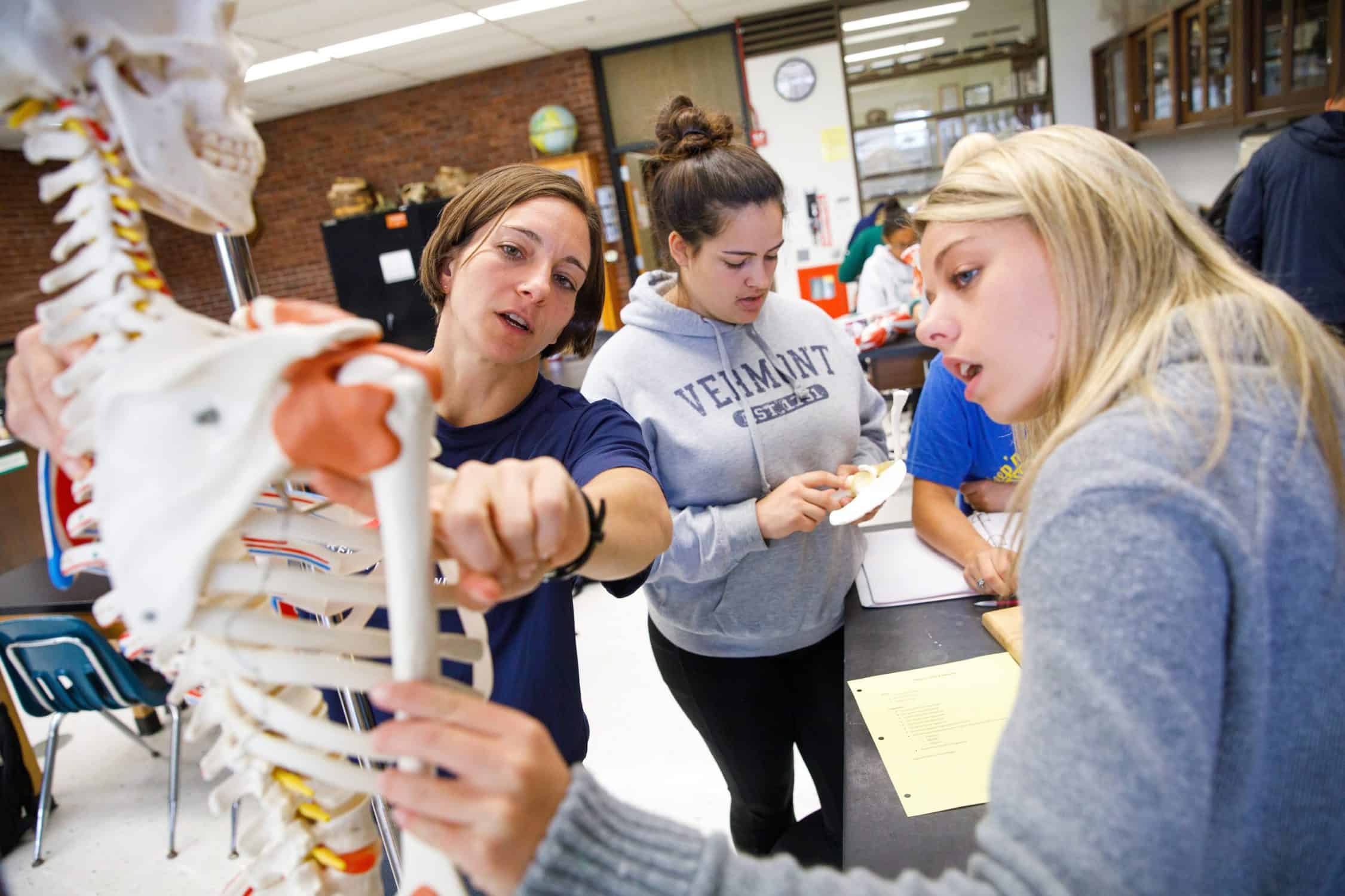 Students learn by examining a medical skeleton with their professor