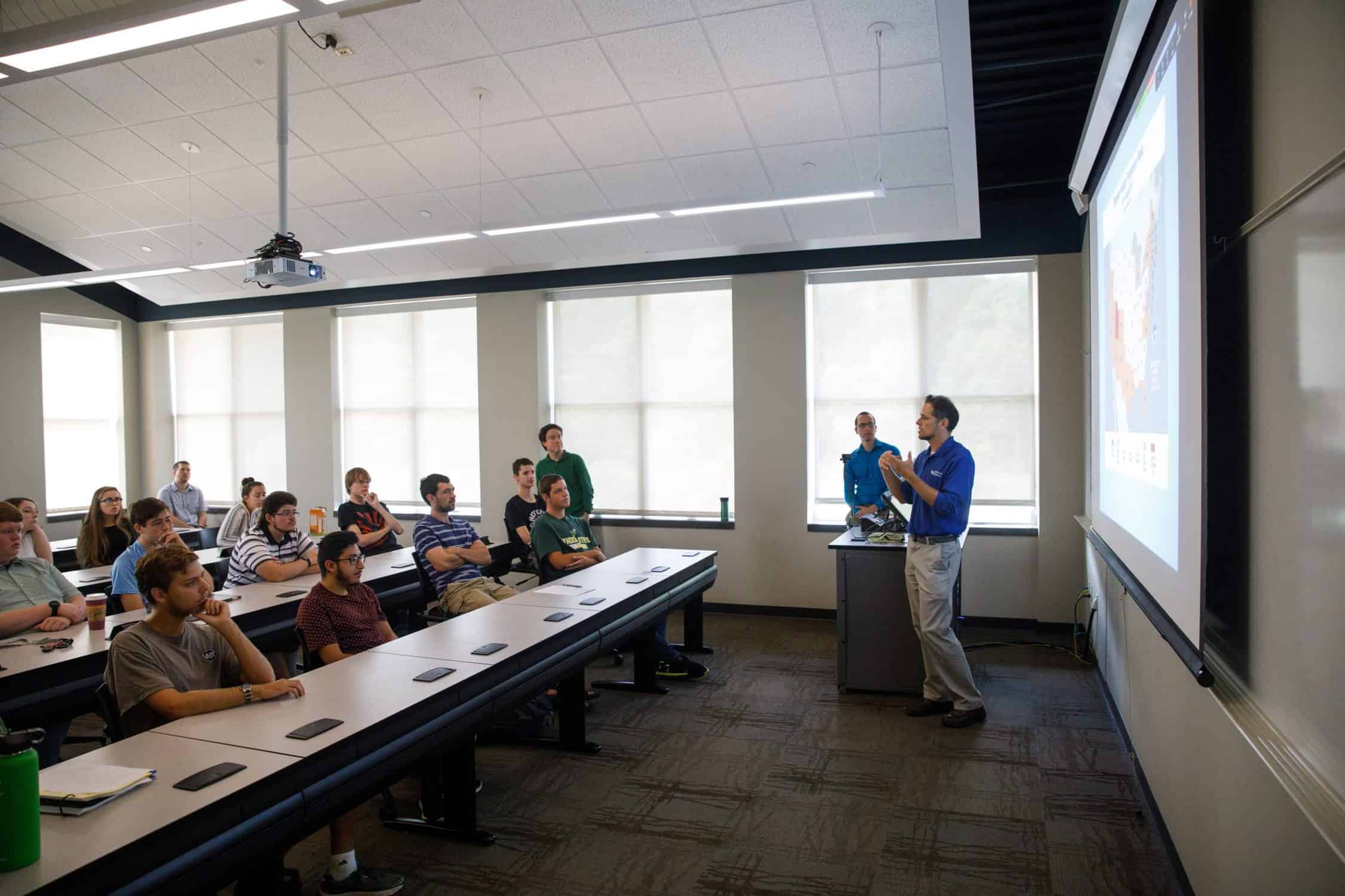 Professor speaks to class in front of a projector screen