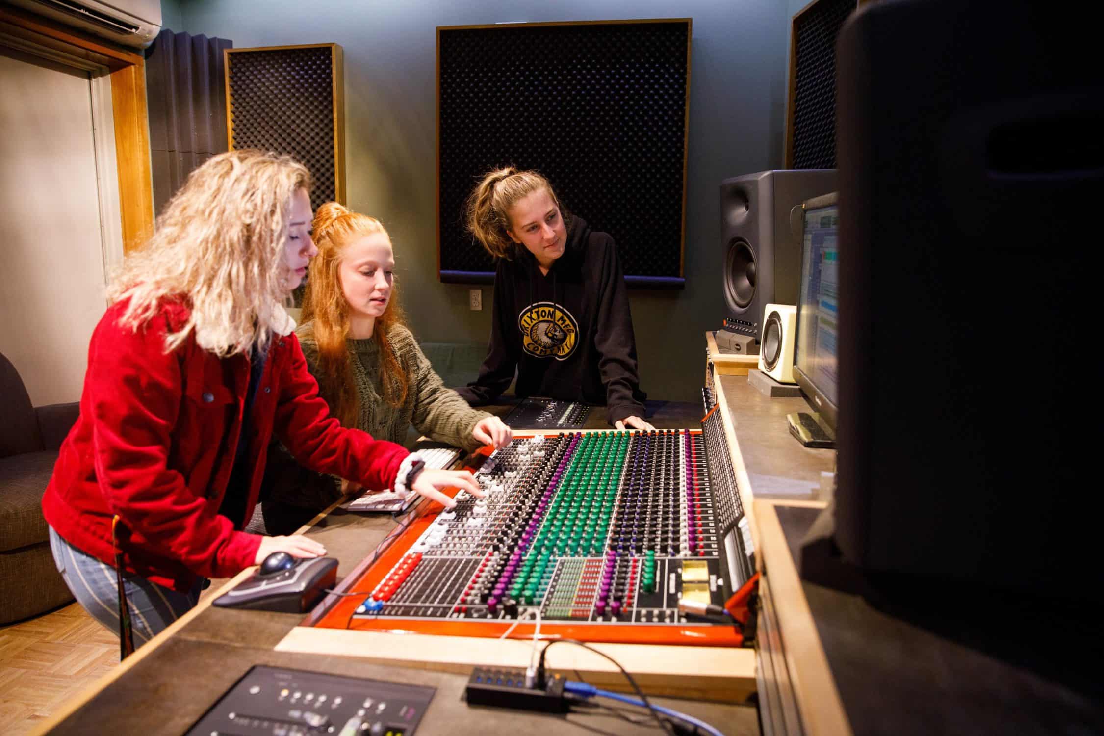 Students gather around the sound board in the recording studio.