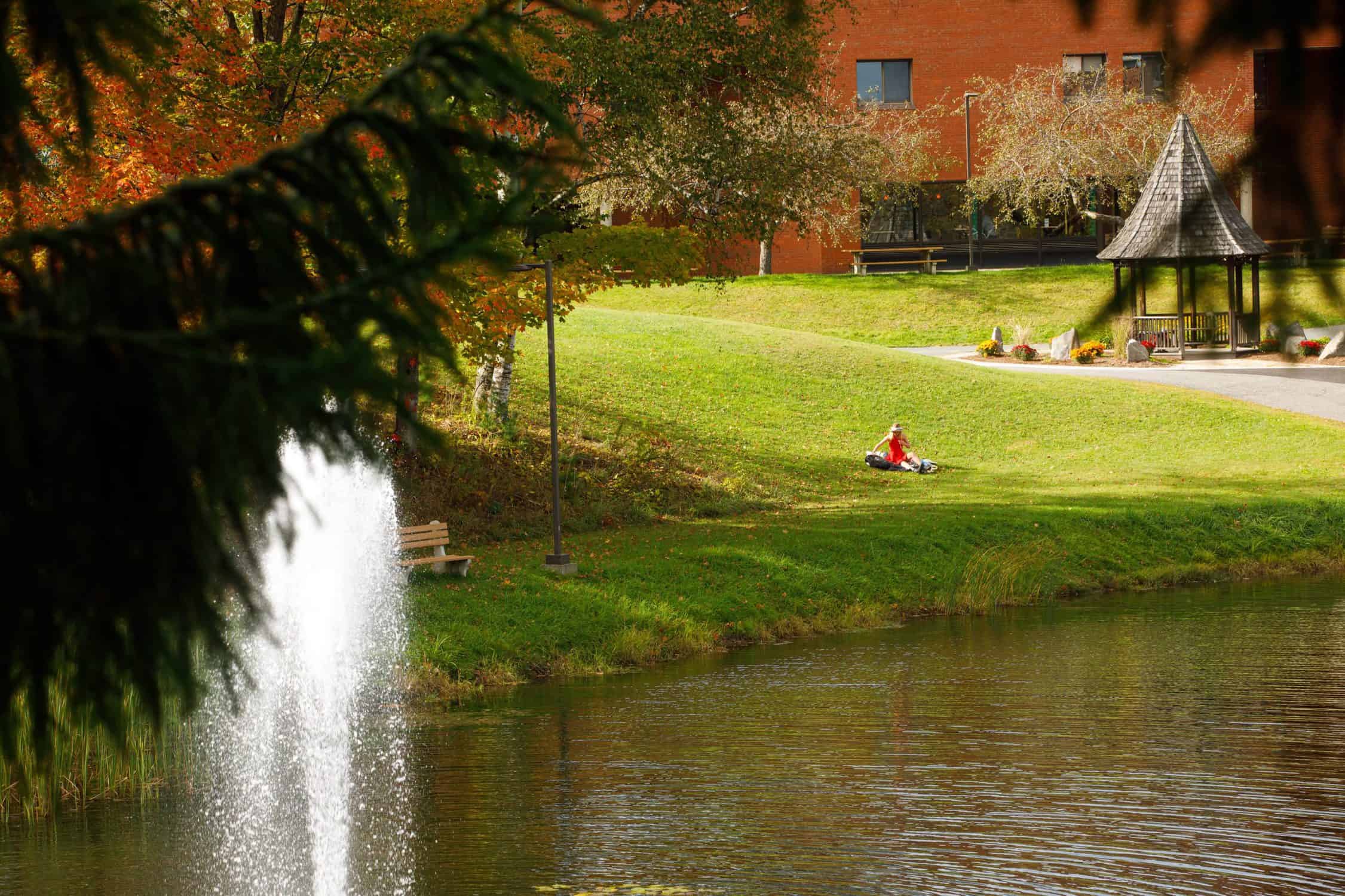 Student relaxes on the grass beside Library Pond