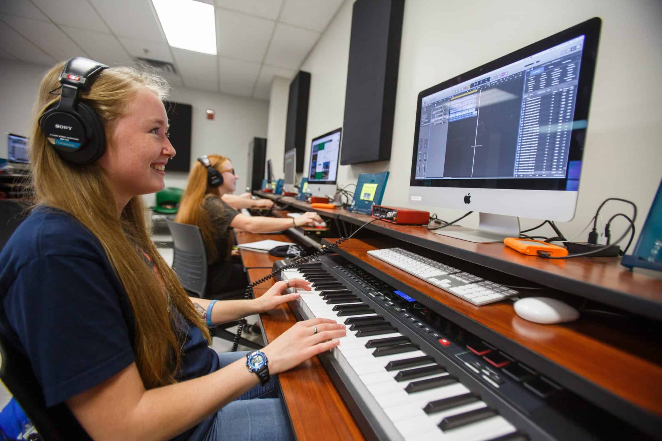 Student looks at computer while creating music with a keyboard