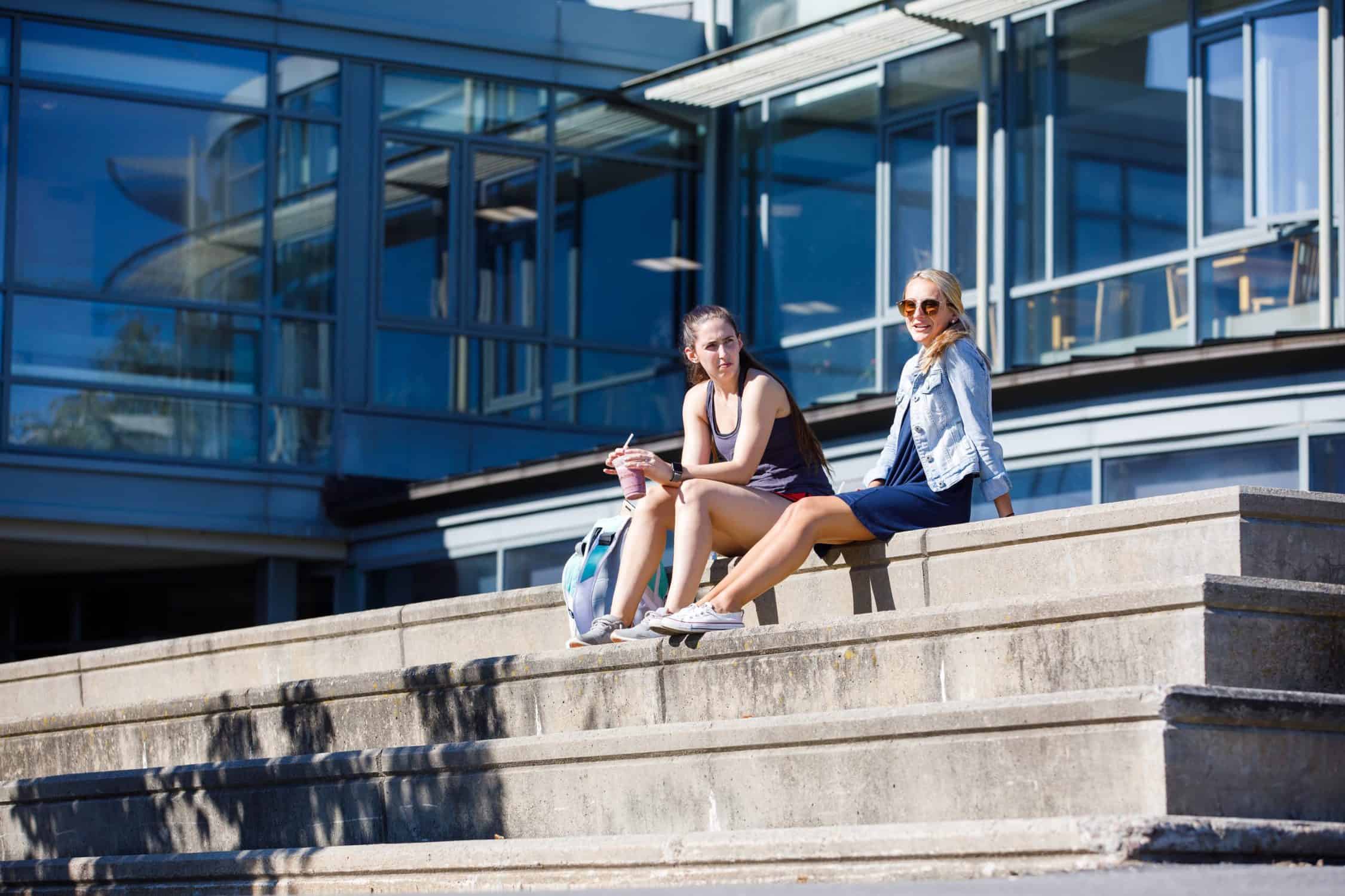 Two students sit on the stairs outside the library