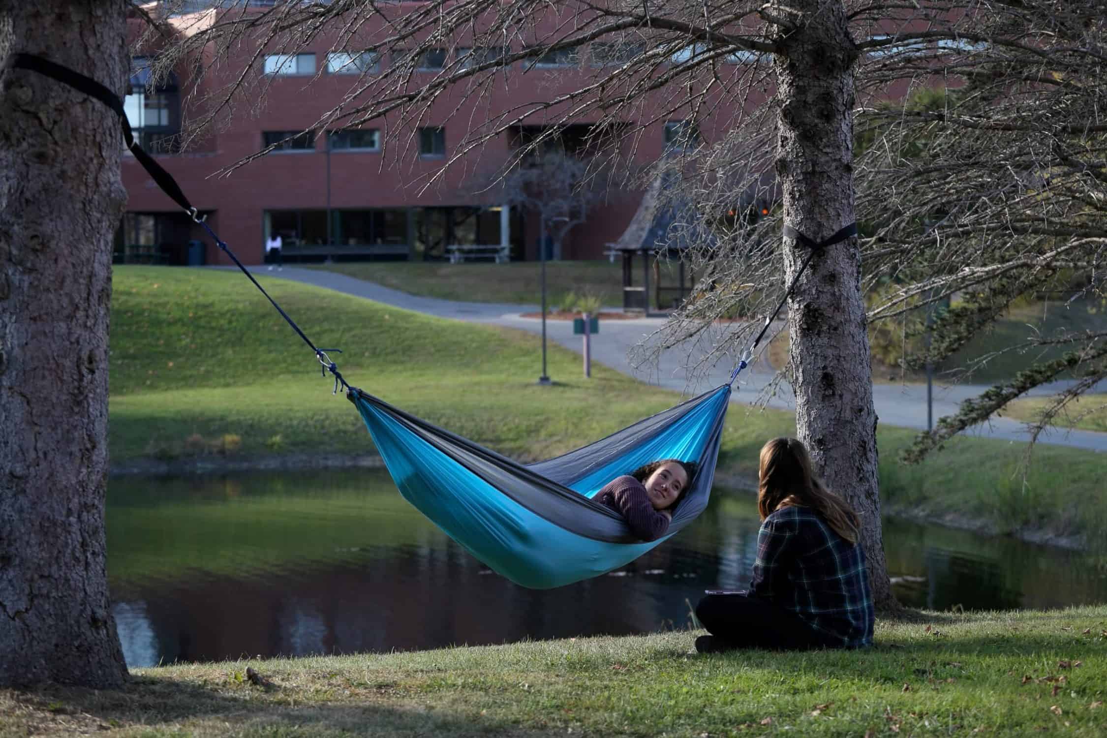 Student relaxes in her hammock on campus while talking to a friend